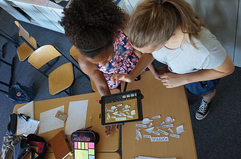 Zwei Mädchen filmen Papierschnipsel mit iPad ab