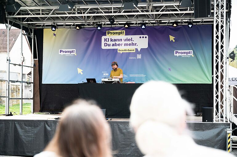 Blick auf eine Bühne, wo ein DJ am Mischpult steht