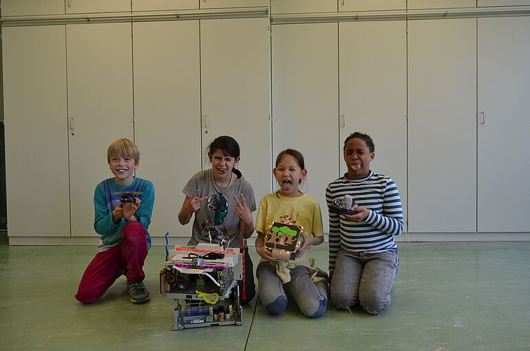eine Gruppe von 4 Kindern präsentiert ihren Roboter aus Elektroschrott und ziehen dabei Grimassen