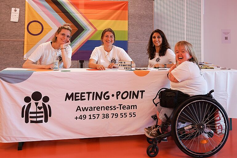 drei Frauen sitzen an einem Meeting Point Awareness Team und im Vordergrund sitzt eine Frau im Rollstuhl 