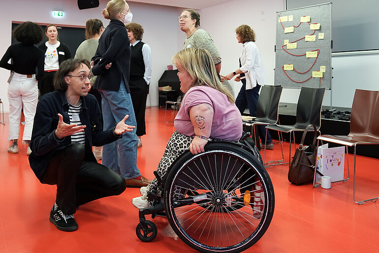 Publikum ca. 100 Personen von oben fotografiert, auf der Buehne sitzen fünf Personen