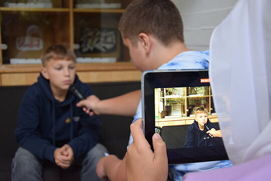 Zwei Jugendliche mit Mikro im Gespräch, ein Jugendlicher filmt mit Tablet